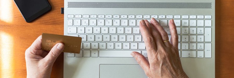 Computer-Tastatur und tippende Hand, die andere Hand hält eine Geldkarte