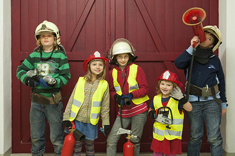 5 Kinder mit Feuerwehrhelmen, Feuerlöschern und Warnwesten.