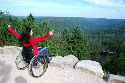 <p>
	Eine Rollstuhlfahrerin genießt die Aussicht auf die Berge und Täler des Schwarzwaldes.</p>
