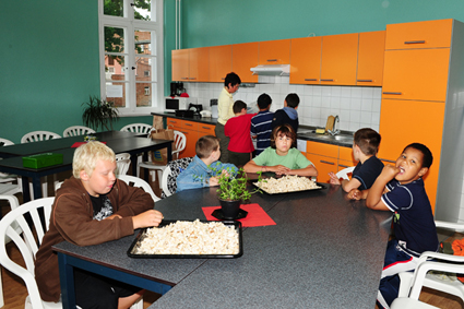 Gemeinsame Mahlzeit: Einige Kinder warten schon am Tisch, während andere noch mit einer Betreuerin an der Küchenzeile stehen.