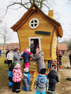 Auf dem Foto ist ein Holzhaus zu sehen, vor dem mehrere Kleinkinder spielen.