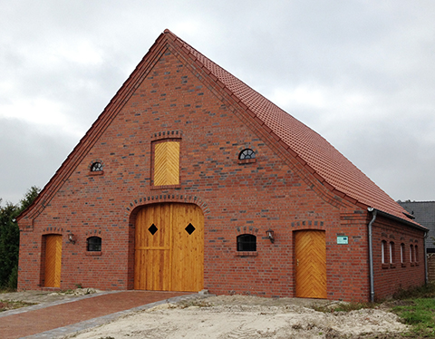 Gebäude aus roten Ziegeln mit mächtigem Spitzdach und hellen Holztüren